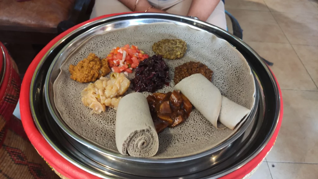 metal plate containing an injera with multiple foods laid upon it in small portions.