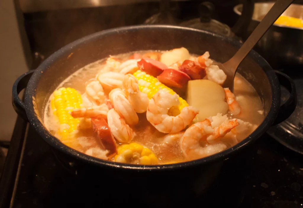 seafood boil on stove top containing shrimp, sausages corn and other vegetables in a broth.